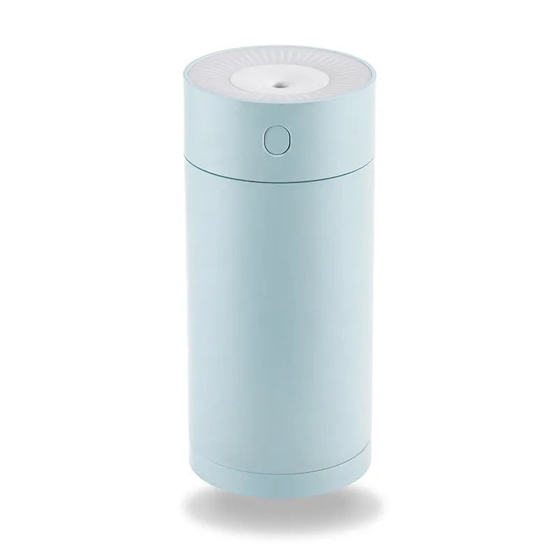 A compact white folding bracket USB humidifier on a desktop next to a laptop, showing its mist output.