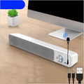 Black desktop computer speaker with USB cable on wooden desk beside monitor