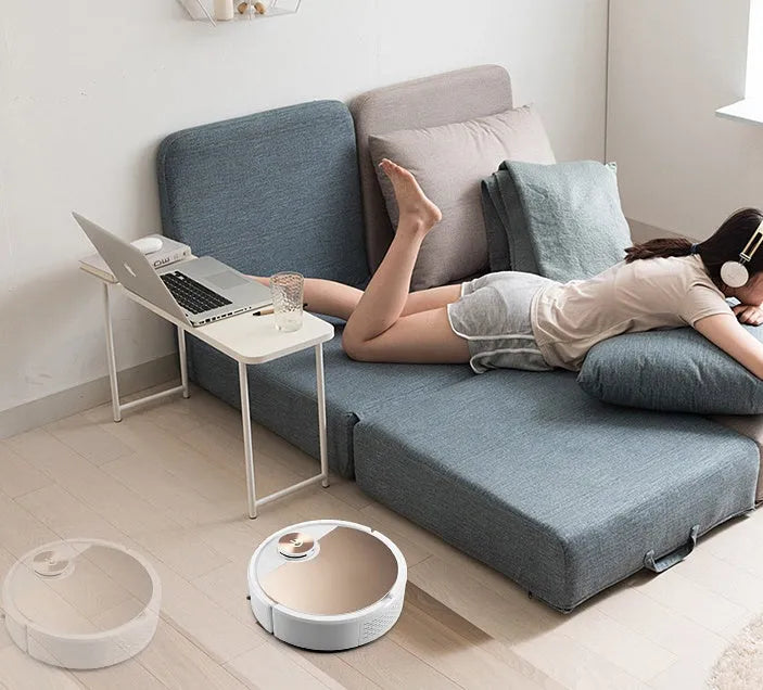Golden and silver robotic vacuum cleaner with remote control on a hardwood floor.