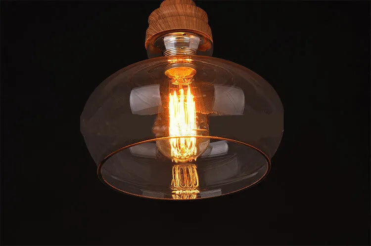 Single head glass pendant light with wood grain finish hanging from ceiling on adjustable cable.