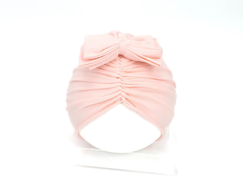 Soft pink knitted acrylic baby bonnet headwrap for a newborn infant.