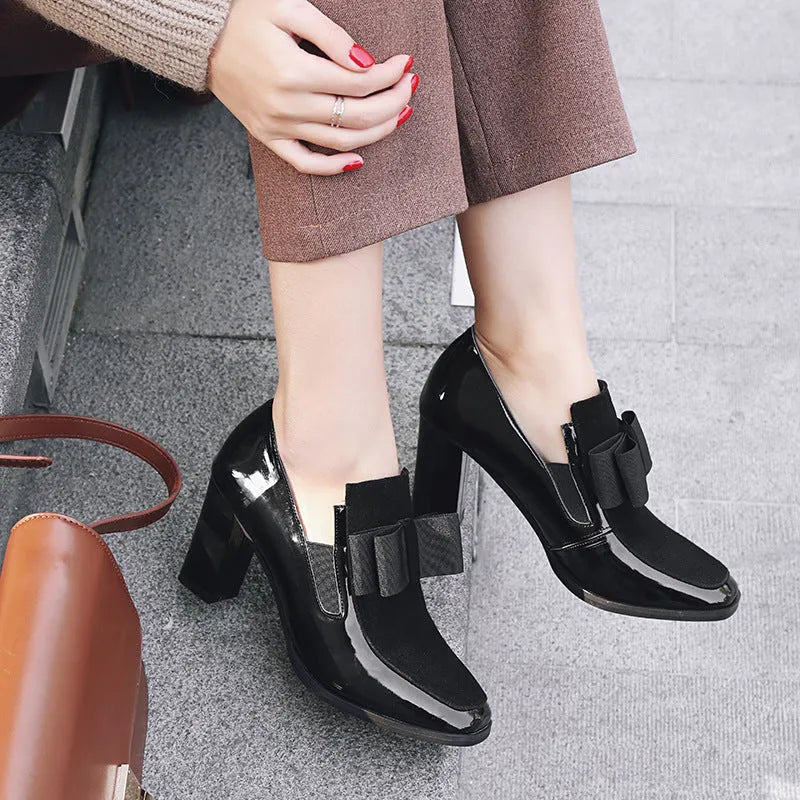 Women's black patent leather high heels with 8cm thick heel and square toe design on wooden floor