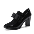 Women's black patent leather high heels with 8cm thick heel and square toe design on wooden floor