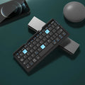 Silver white folding Bluetooth keyboard shown open with stand holding a smartphone, and folded next to a ruler for scale.