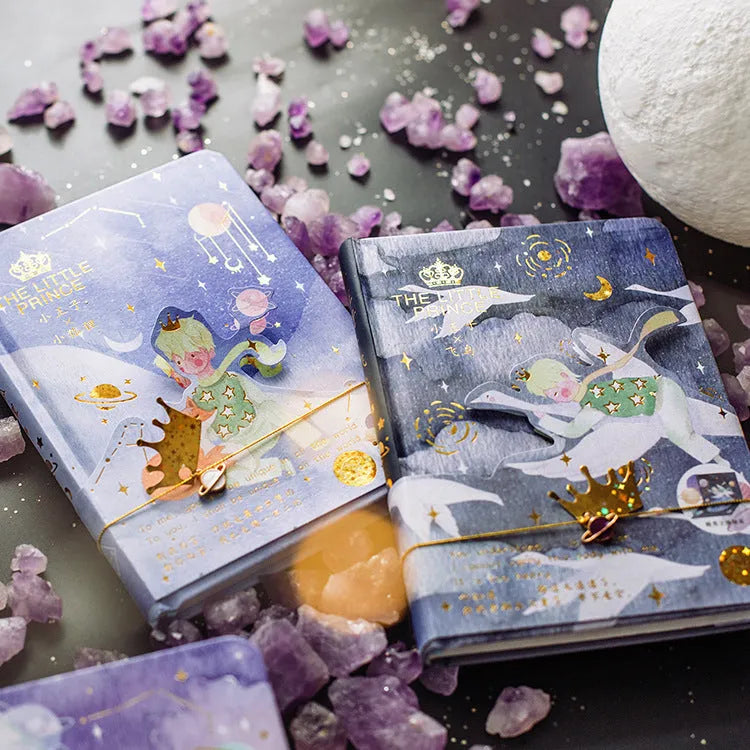 A5 hardback notebook with The Little Prince cartoon illustration cover, open on a flat surface.