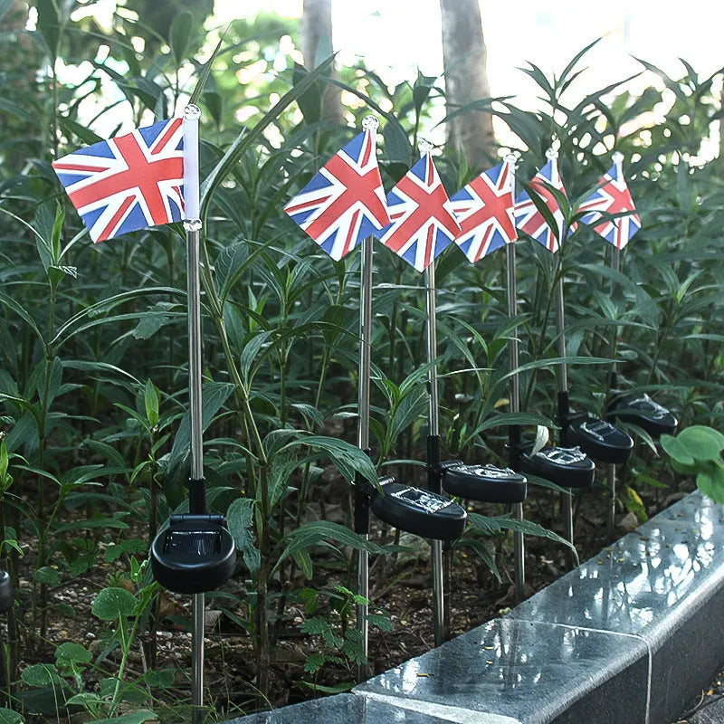 Solar-powered garden flag light with a stainless steel pole displaying a British flag design at night.