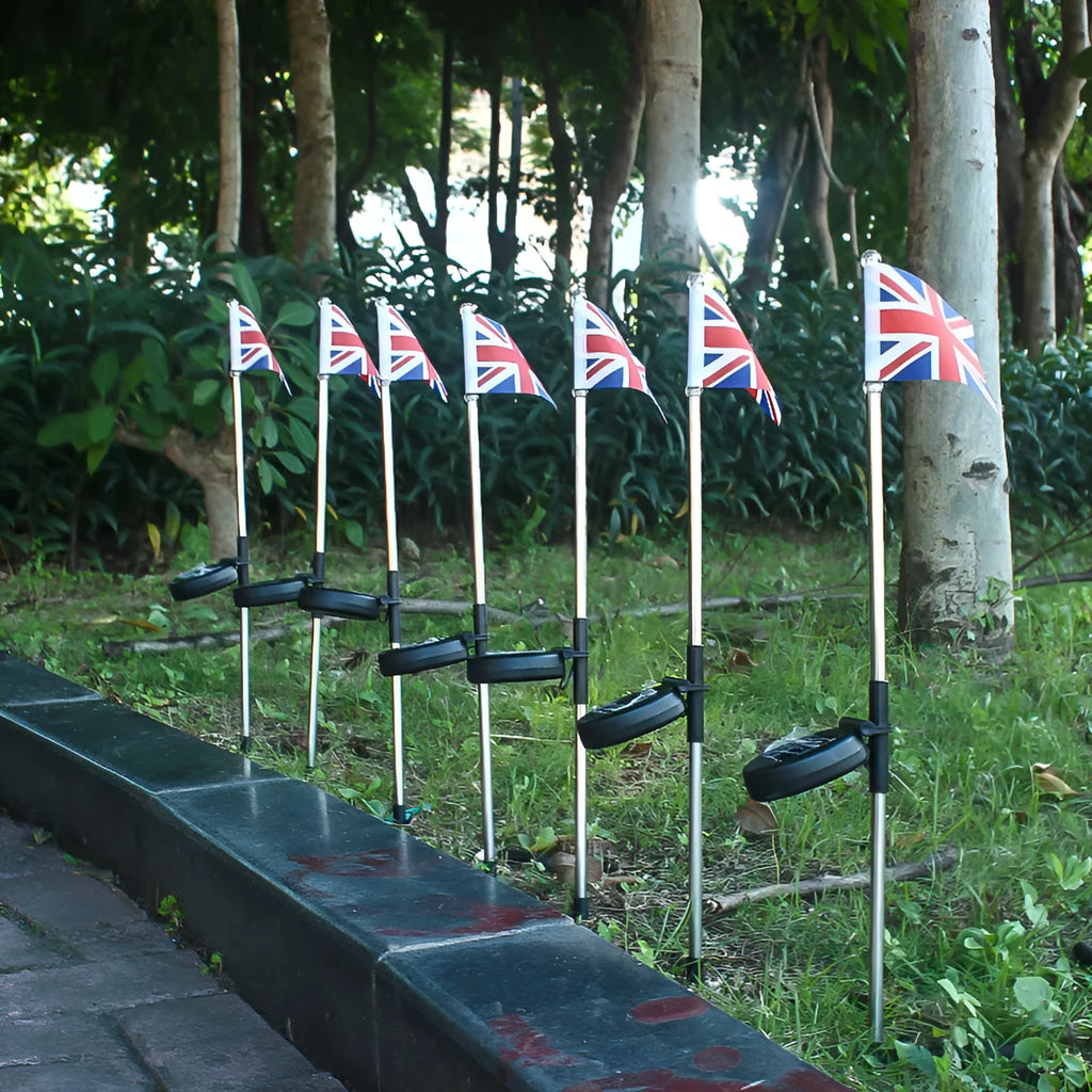 Solar-powered garden flag light with a stainless steel pole displaying a British flag design at night.