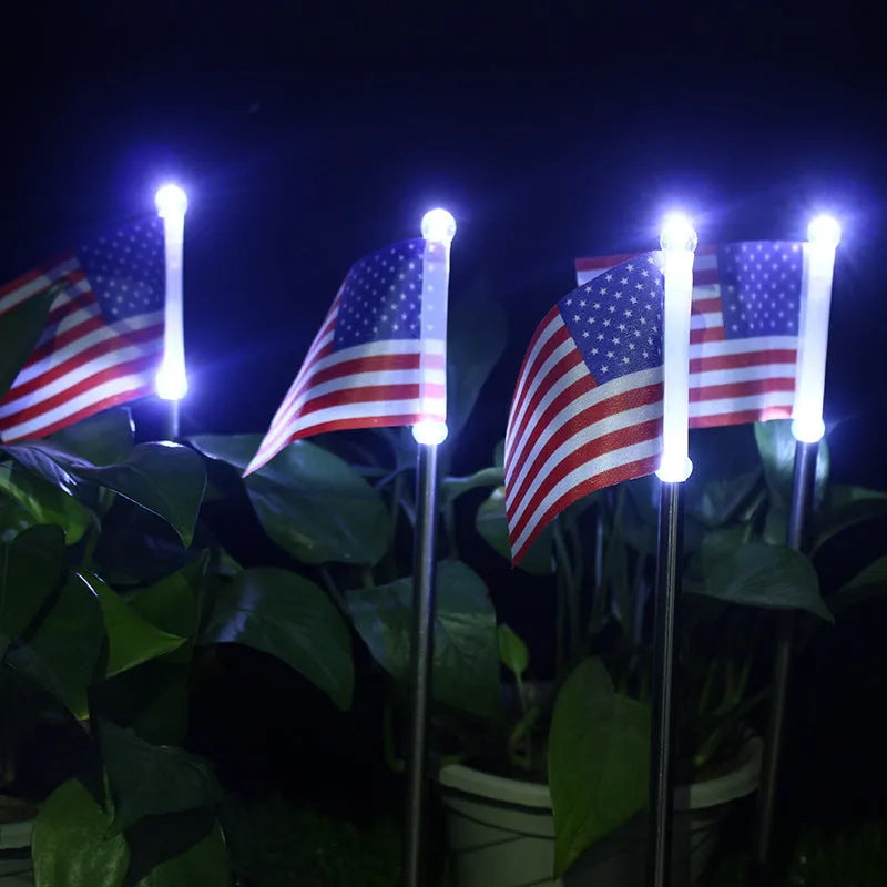 Solar-powered garden flag light with a stainless steel pole displaying a British flag design at night.