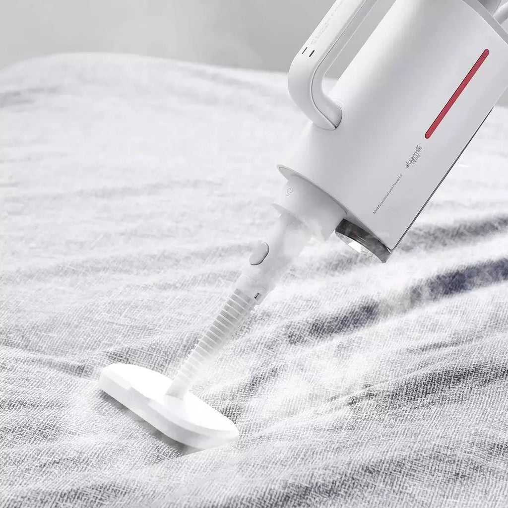 White Deerma DEM-ZQ610 steam cleaner main unit with brush heads and attachments on a table.
