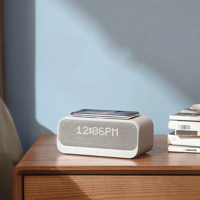 Anker Soundcore white Bluetooth speaker alarm clock with wireless charging pad on a bedside table.