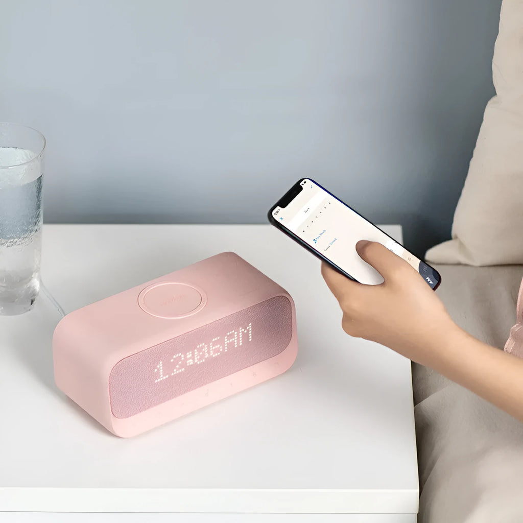 Anker Soundcore white Bluetooth speaker alarm clock with wireless charging pad on a bedside table.