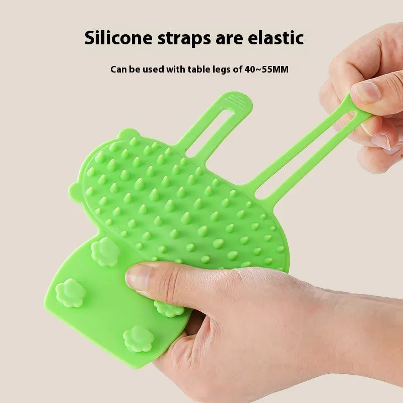 Black silicone cat grooming comb with adjustable strap attached to a table leg, showing rounded teeth for hair removal