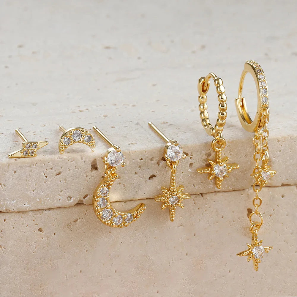 XINGX set of six gold chain tassel and zircon stud drop earrings laid out on a dark surface