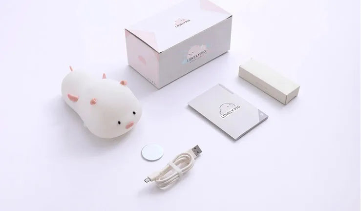 Cute pink silicone pig night light with sleeping design on a bedside table.