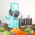 Blue green round mandoline slicer with three stainless steel drum blades and a suction base on a kitchen counter.