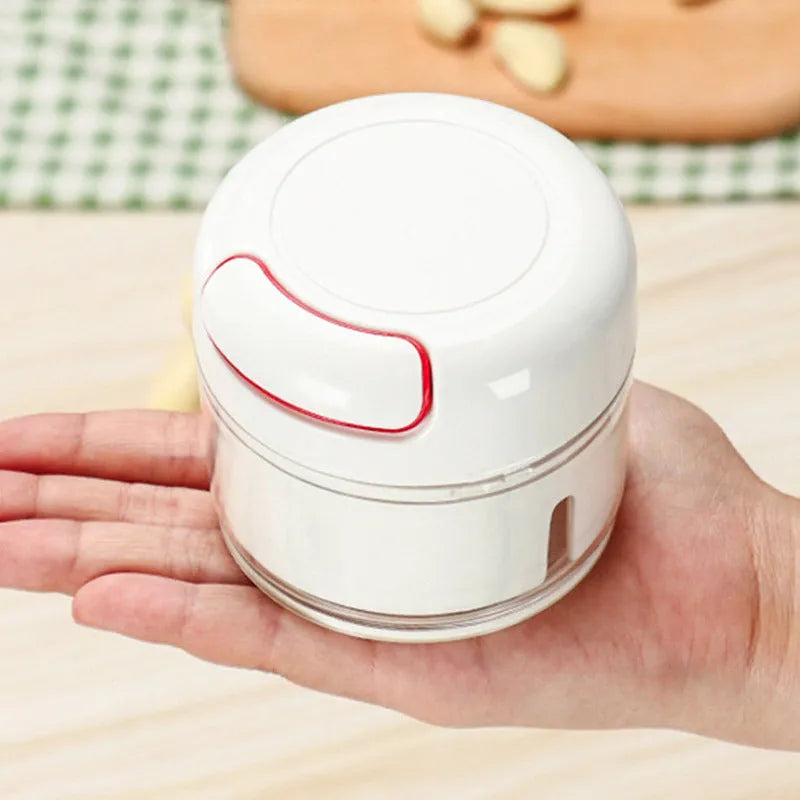 White manual food chopper with stainless steel blades on a magnetic holder, shown with chopped vegetables.