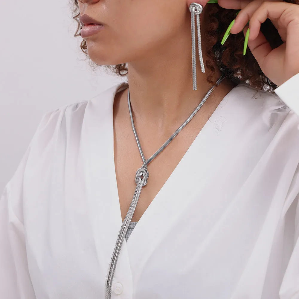Gold titanium steel necklace with tassel pendant and matching earrings on dark background