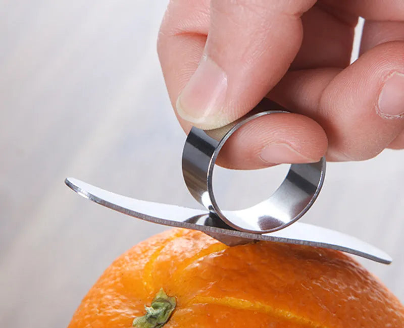 A silver stainless steel finger-ring style citrus peeler for oranges and pomelo on a kitchen surface.