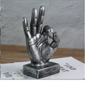 Bronze and silver resin hand gesture ornaments on a wooden desk, showing like, ok, and scissors hand signs.