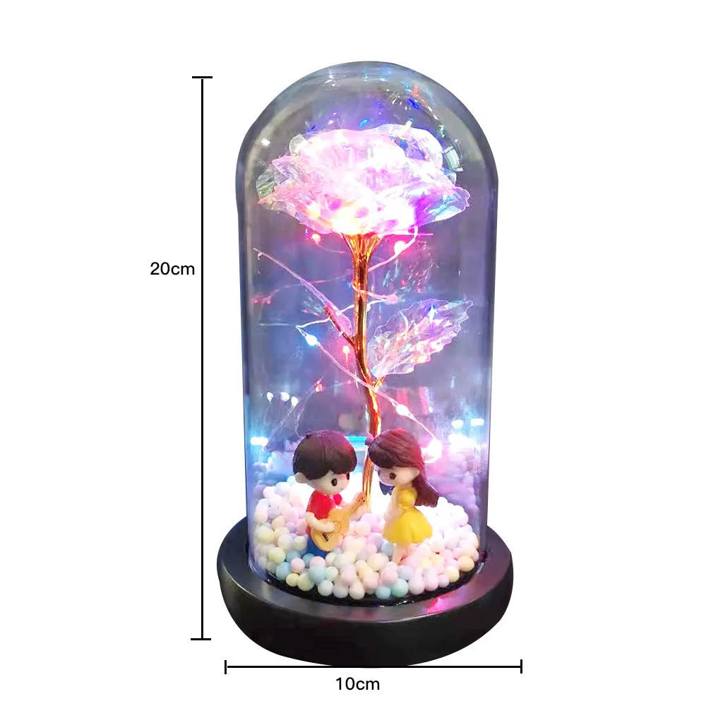 Gold artificial roses inside a clear glass dome ornament with LED lights and decorative accessories.