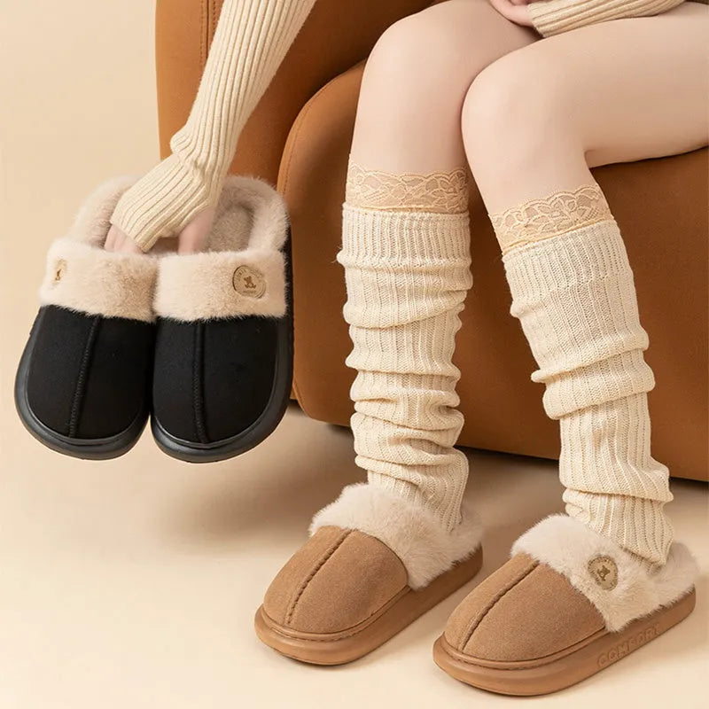 Plush slippers in black with fleece lining and non-slip PVC soles, shown on a wooden floor