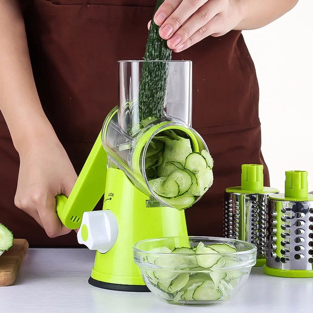 Blue green round mandoline slicer with three stainless steel drum blades and a suction base on a kitchen counter.