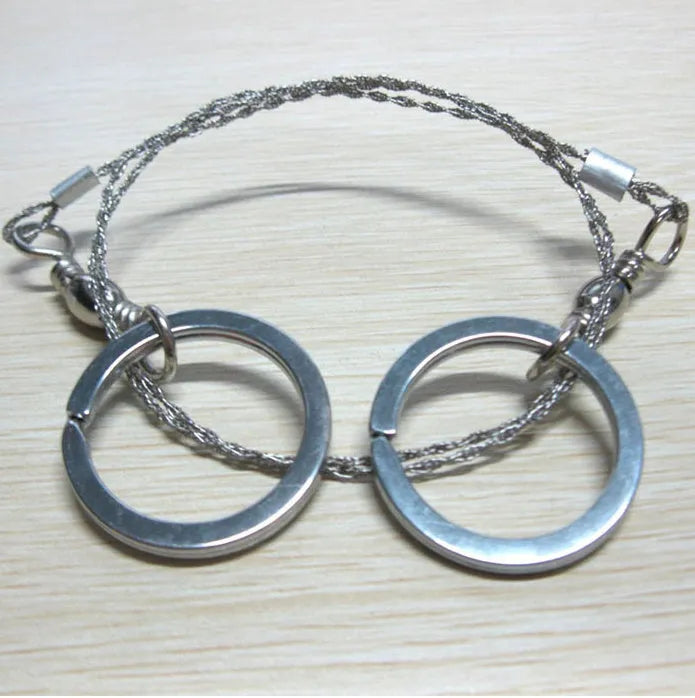 Coiled stainless steel survival wire saw with two black thumb rings, shown next to a ruler showing its 55cm length.