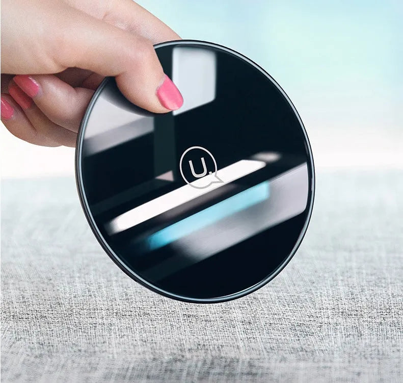 Black and white glass disc wireless charging pad for mobile phones on a wooden table.