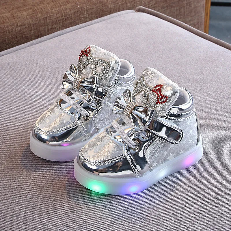 Set of golden, pink, and silvery LED light-up shoe buttons with glitter laces on a trainer.