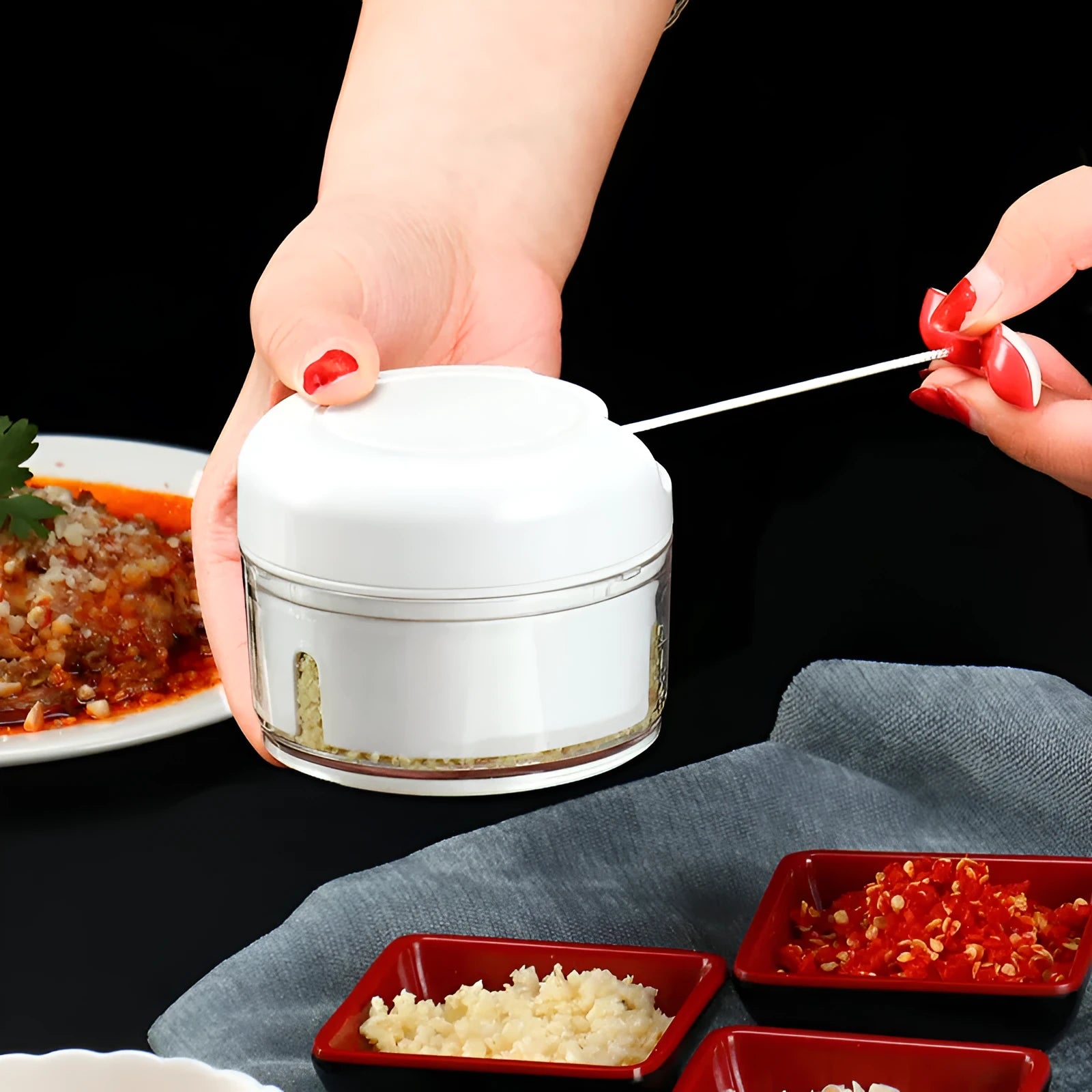 White manual food chopper with stainless steel blades on a magnetic holder, shown with chopped vegetables.
