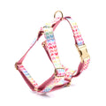 Pink colourful dog harness with heart-shaped stone details and a gold buckle on a white background.