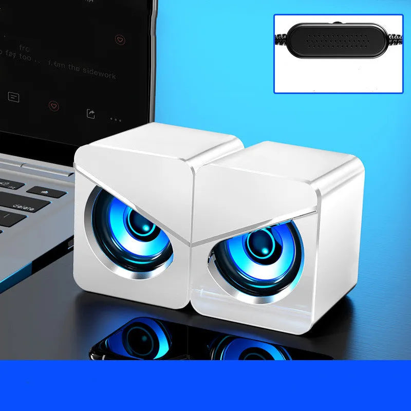 Black and white USB desktop mini speaker with cable next to a laptop computer.