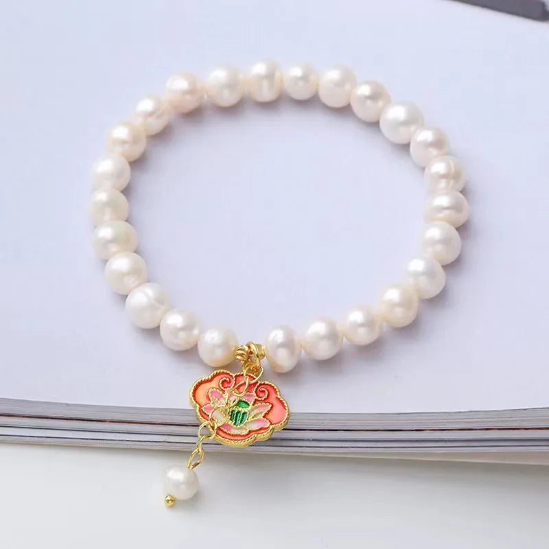 White freshwater pearl and gold electroplated lotus goldfish pendant on an antique style women's bracelet.