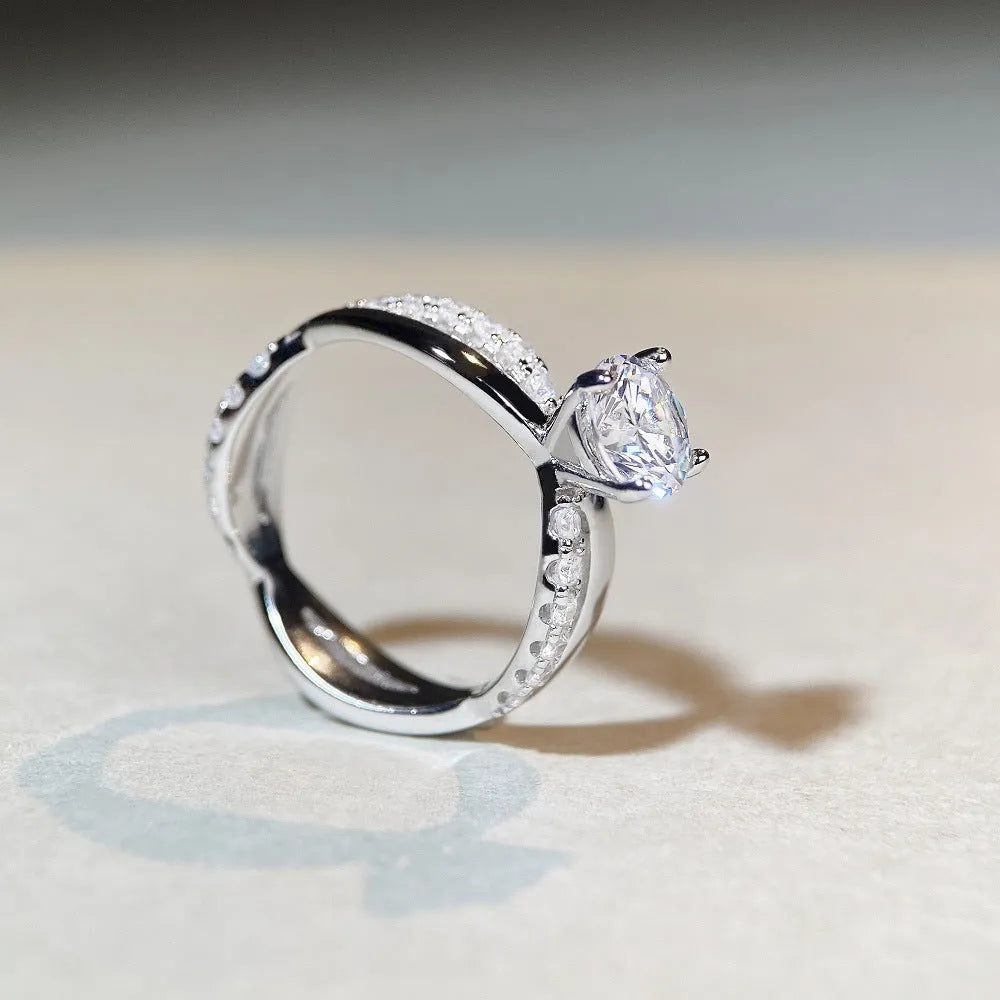 Geometric silver moissanite ring with twisted arm design and four-claw setting, shown in white diamond colour.