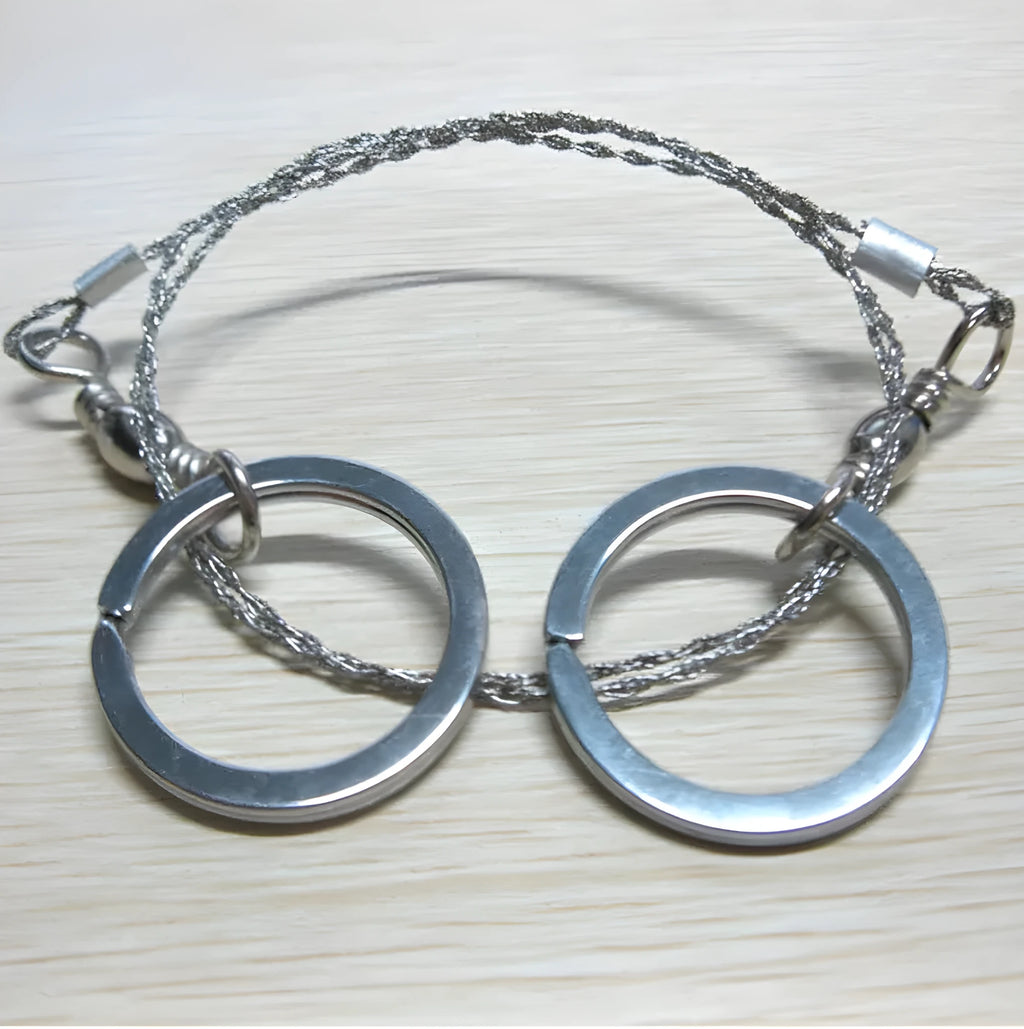 Coiled stainless steel survival wire saw with two black thumb rings, shown next to a ruler showing its 55cm length.
