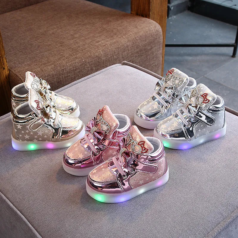 Set of golden, pink, and silvery LED light-up shoe buttons with glitter laces on a trainer.