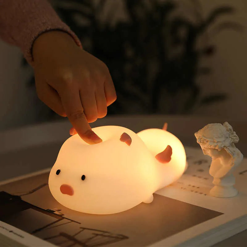 Cute pink silicone pig night light with sleeping design on a bedside table.