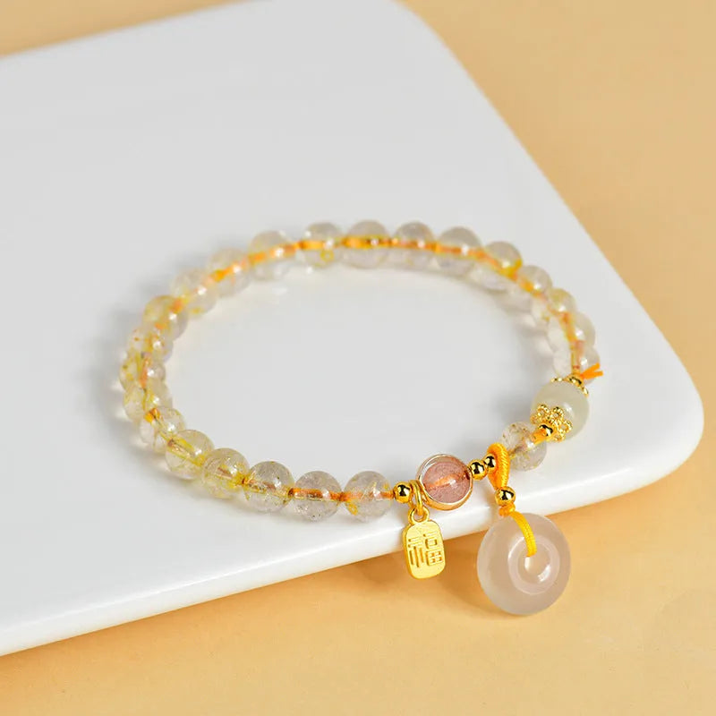 Gold rutilated quartz crystal bracelet with a safety buckle and a small rectangular blessing card pendant.