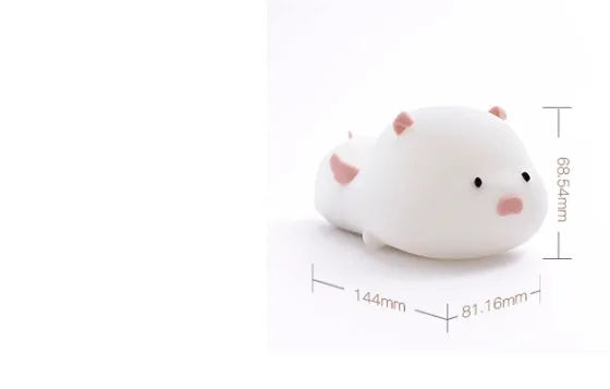 Cute pink silicone pig night light with sleeping design on a bedside table.