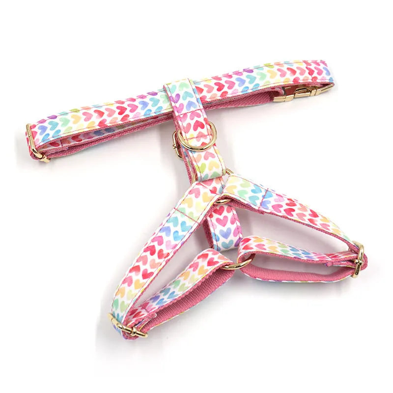 Pink colourful dog harness with heart-shaped stone details and a gold buckle on a white background.