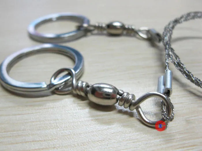 Coiled stainless steel survival wire saw with two black thumb rings, shown next to a ruler showing its 55cm length.