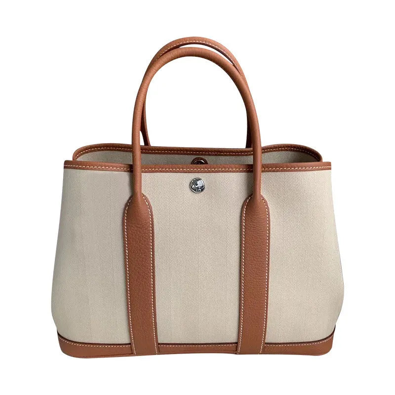 Women's canvas tote bag with leather accents showing internal zipper compartments and soft carry handle