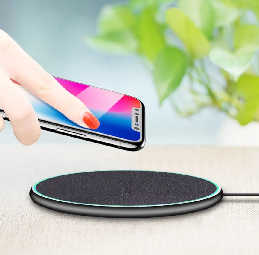 Black Quick Qi wireless charging pad for iPhone 11 on a wooden desk.