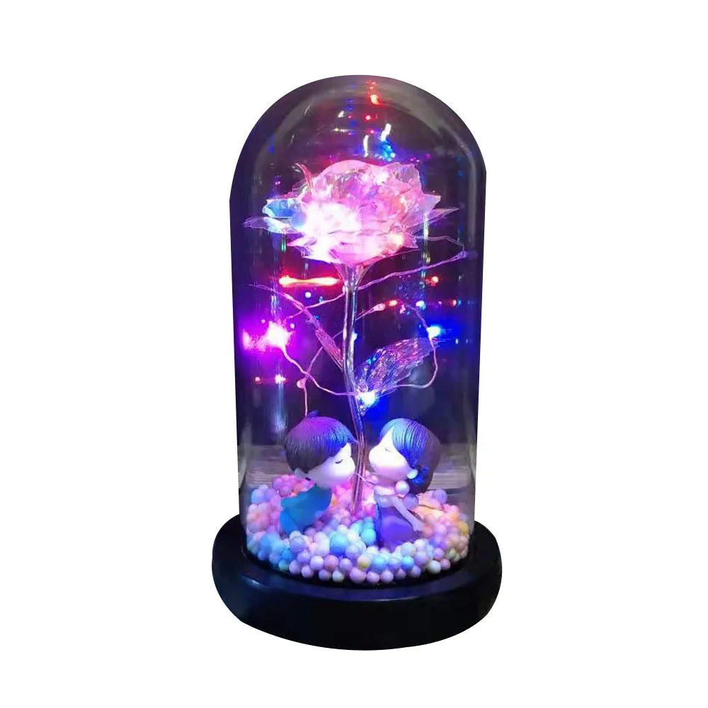 Gold artificial roses inside a clear glass dome ornament with LED lights and decorative accessories.