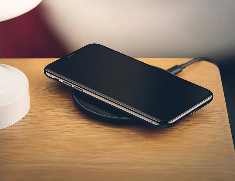 Black and white glass disc wireless charging pad for mobile phones on a wooden table.