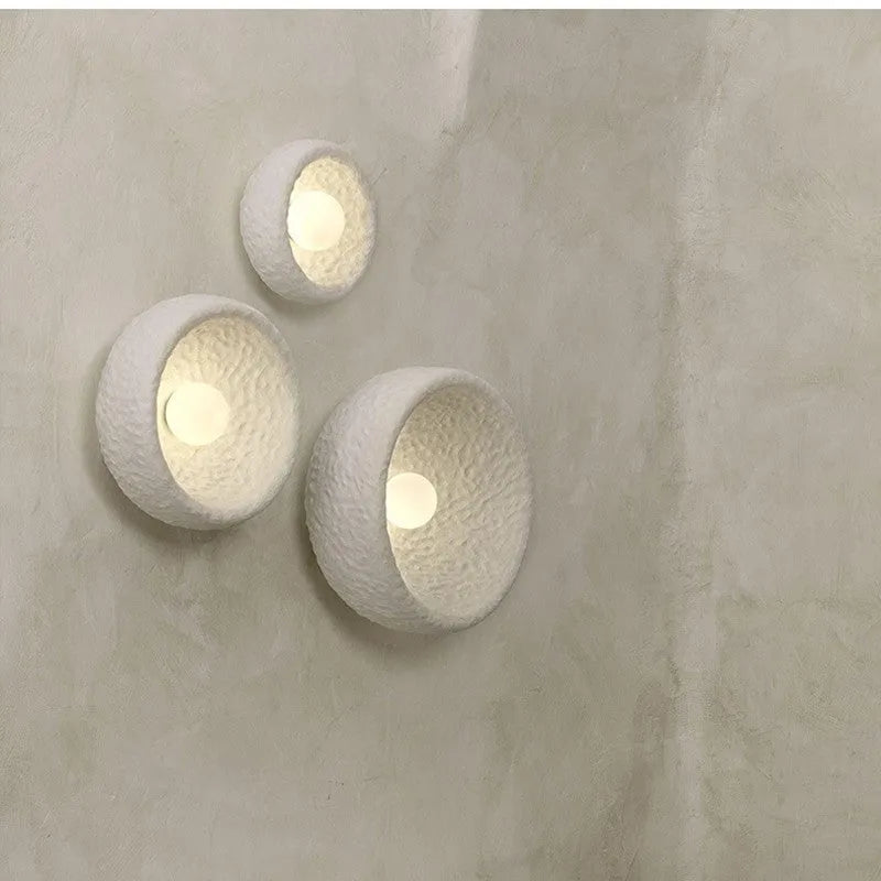 Japanese-style simple white resin wall lamp emitting warm light on a plain wall.