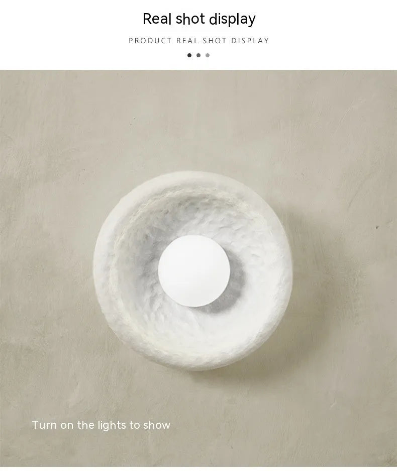 Japanese-style simple white resin wall lamp emitting warm light on a plain wall.