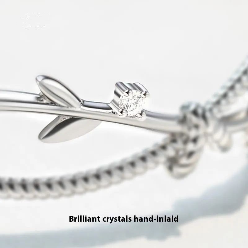 Close-up of an adjustable white gold coloured copper bracelet with a twisted branch and sprout design.