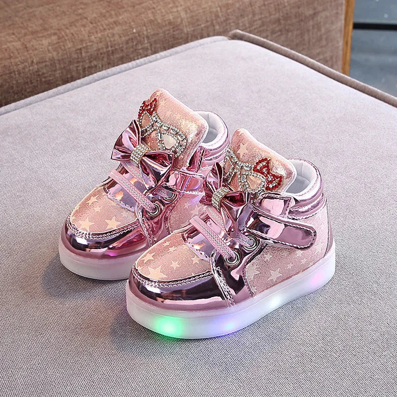 Set of golden, pink, and silvery LED light-up shoe buttons with glitter laces on a trainer.