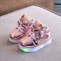 Set of golden, pink, and silvery LED light-up shoe buttons with glitter laces on a trainer.